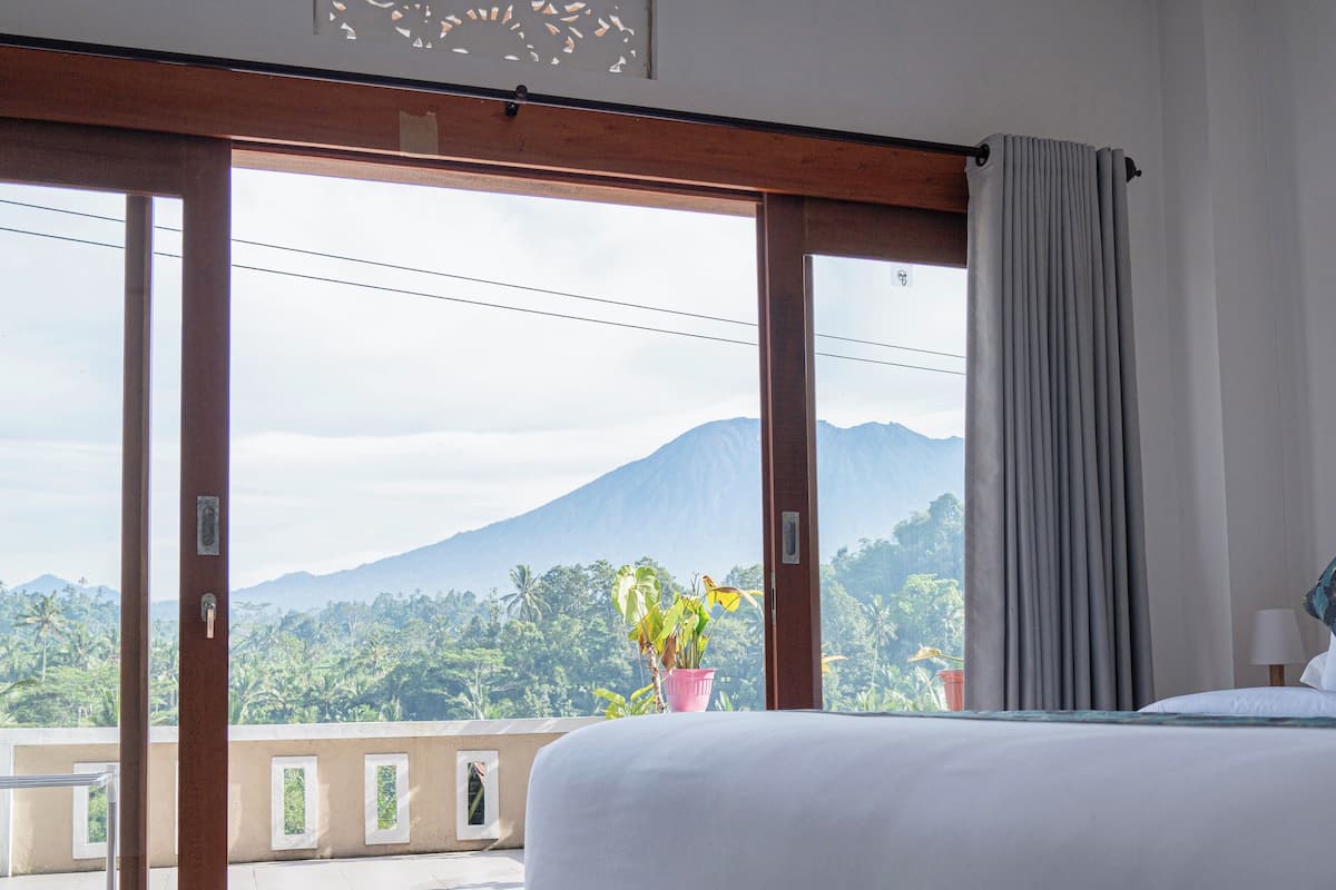 Habitación de hotel con una cama grande, vista a una montaña y un balcón con una planta en maceta.