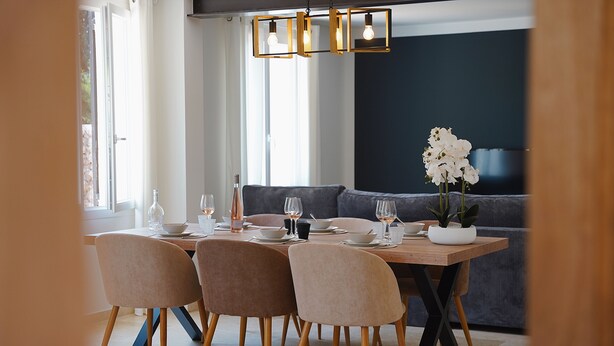 A dining area with a wooden table, four chairs, a sofa, and a potted plant.