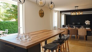 A modern kitchen with a wooden island, bar stools, and a dining area with a black TV and seating.