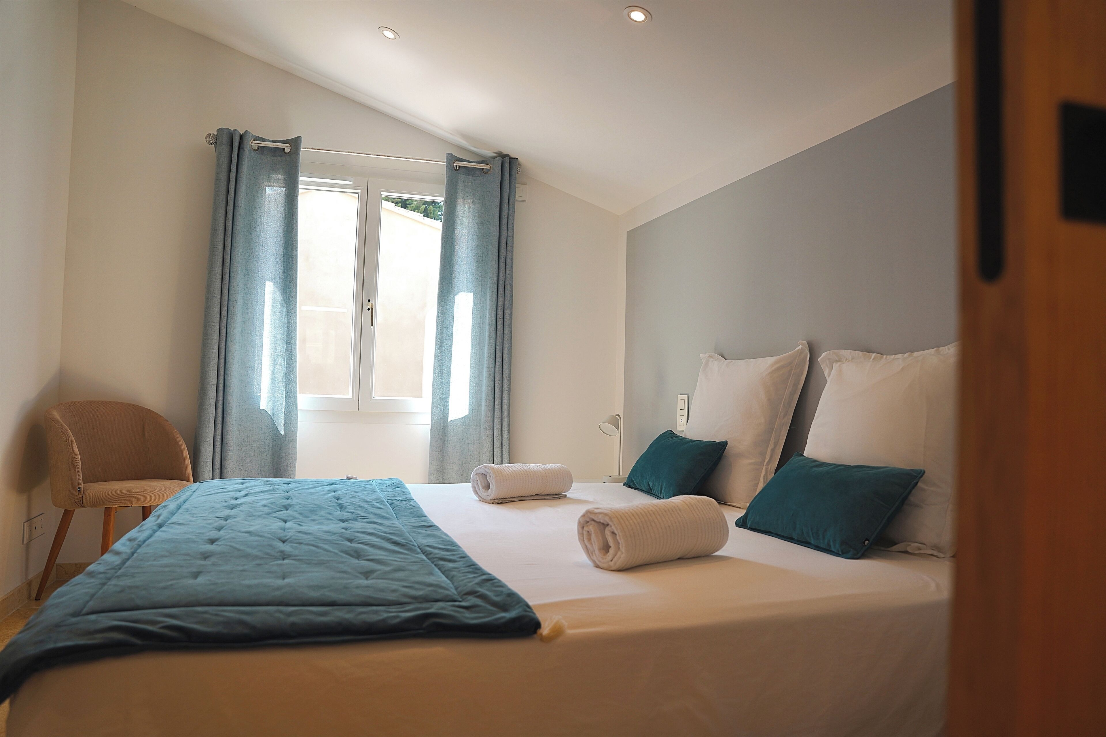 A bedroom with a bed, a chair, a desk, and a window with curtains.