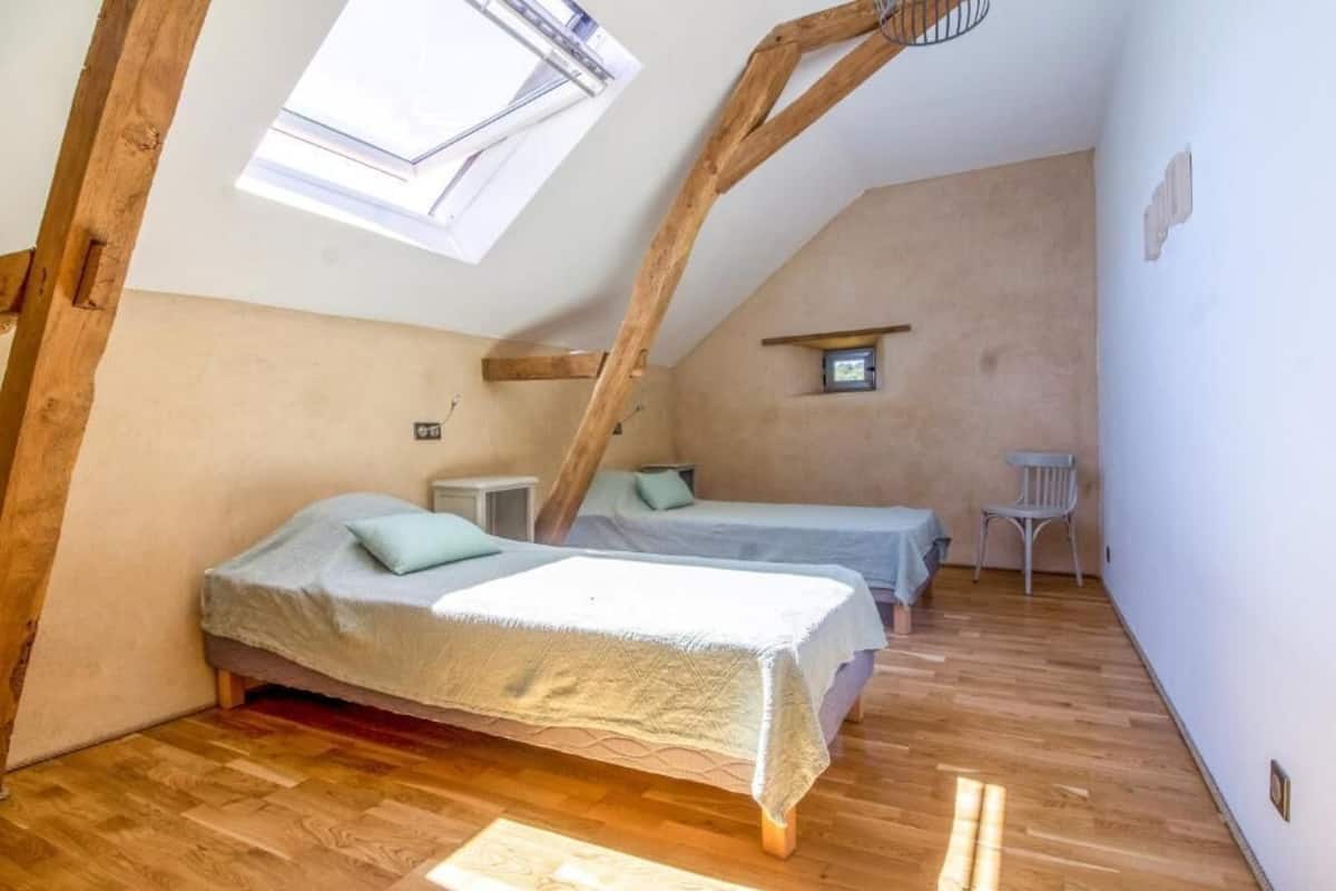 A small, cozy attic bedroom with two beds, a small table, and a chair.