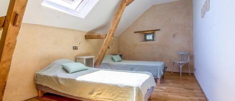 Une petite chambre mansardée, chaleureuse et accueillante, avec deux lits, une petite table et une chaise.