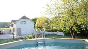 Una piscina con escalera, rodeada por un edificio blanco y un árbol.