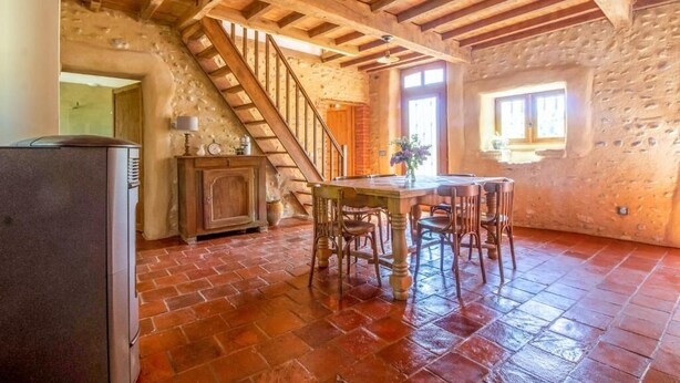 Una cocina rústica con una escalera de madera, una mesa de comedor con sillas y un refrigerador.
