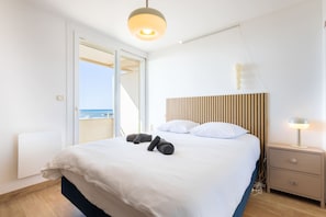 A bedroom with a bed, a bedside lamp, a wooden headboard, and a view of the sea.