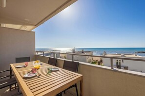 A balcony with a wooden table set for dining, overlooking a beach and the ocean.