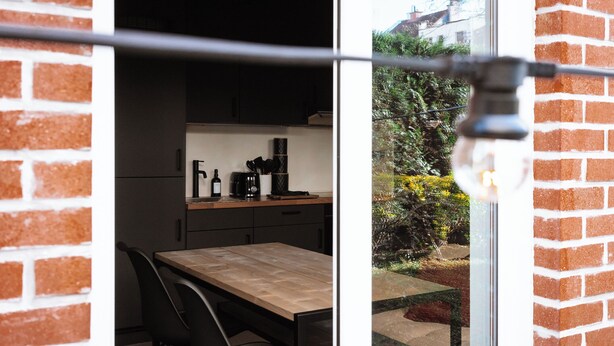 Een keuken met een houten tafel en stoelen, een koffieapparaat en een raam met uitzicht op een tuin.