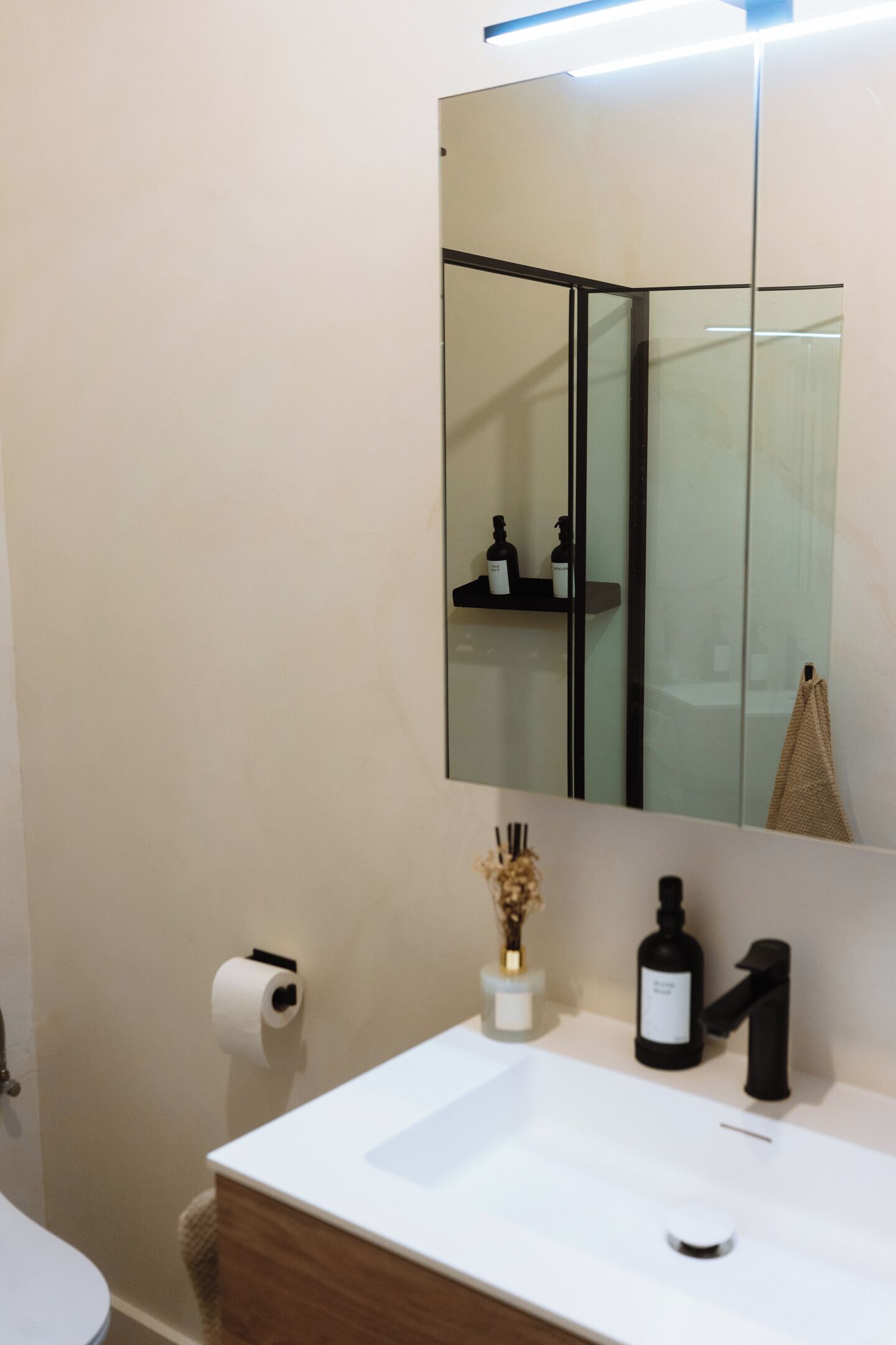Une salle de bain avec un lavabo blanc, un miroir, un porte-serviettes et un support à papier toilette.