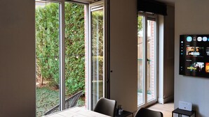 Een kamer met een schuifdeur naar een tuin, een flatscreen televisie aan de muur en een klein tafeltje met een laptop.