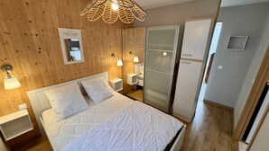 A bedroom with a bed, bedside tables, a mirror, a wardrobe, and a hanging light fixture. - Romantic Cocoon With Private Garden (Mont-Dore)