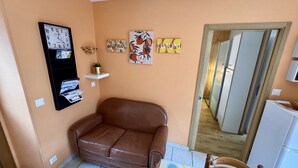 A living room with a brown leather sofa, a wall clock, a small shelf with a plant, and three framed pictures on the wall. - Romantic Cocoon With Private Garden (Mont-Dore)