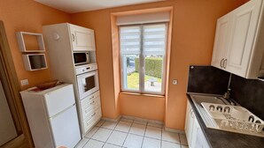 A compact kitchen with white appliances, a window with a view of a garden, and a sink with a faucet. - Romantic Cocoon With Private Garden (Mont-Dore)