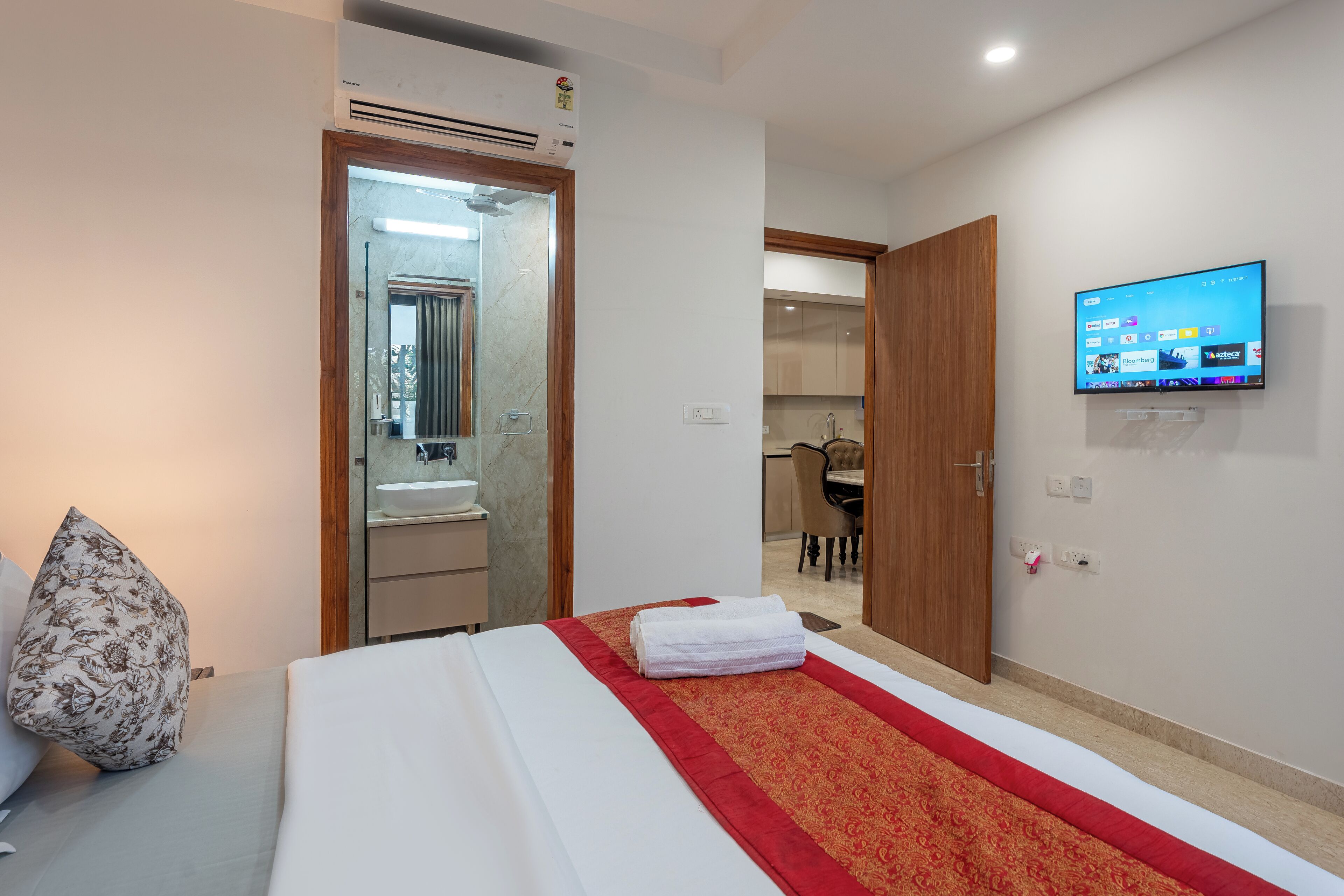 Une chambre d’hôtel avec un lit, un téléviseur fixé au mur et une salle de bain visible à travers une porte ouverte.