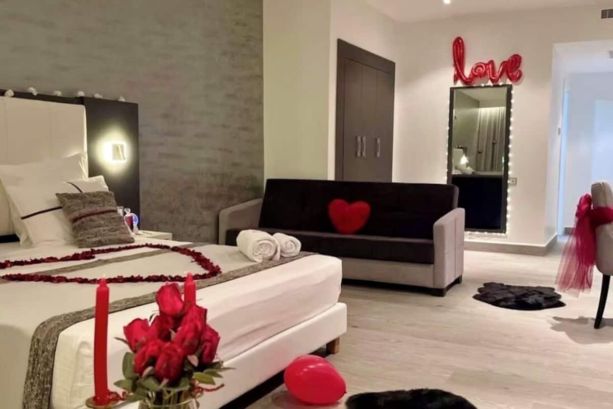A modern bedroom with a bed, a sofa, a mirror, and a decorative heart on the wall.