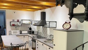 A compact kitchen with a dining area, wooden beams, a black stove, and a clock. - La Chapelle - Le Mont Dore 2 Pers (Mont-Dore)