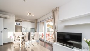 Een moderne woonkamer met een flatscreen-tv, een eethoek met een tafel en stoelen, en een keuken met een magnetron en kastjes.