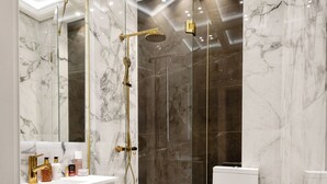Een moderne badkamer met een douche met glazen wand, marmeren vloer en een wit toilet.