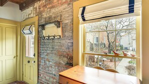 A room with a wooden desk, a chair, a yellow door, a brick wall, and a window with a view of a yard and chickens.