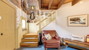 A staircase with wooden steps and a brick wall, a leather armchair with a cushion, a bench, and a framed picture on the wall.