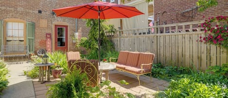 A patio with outdoor furniture, a red umbrella, and a brick house.