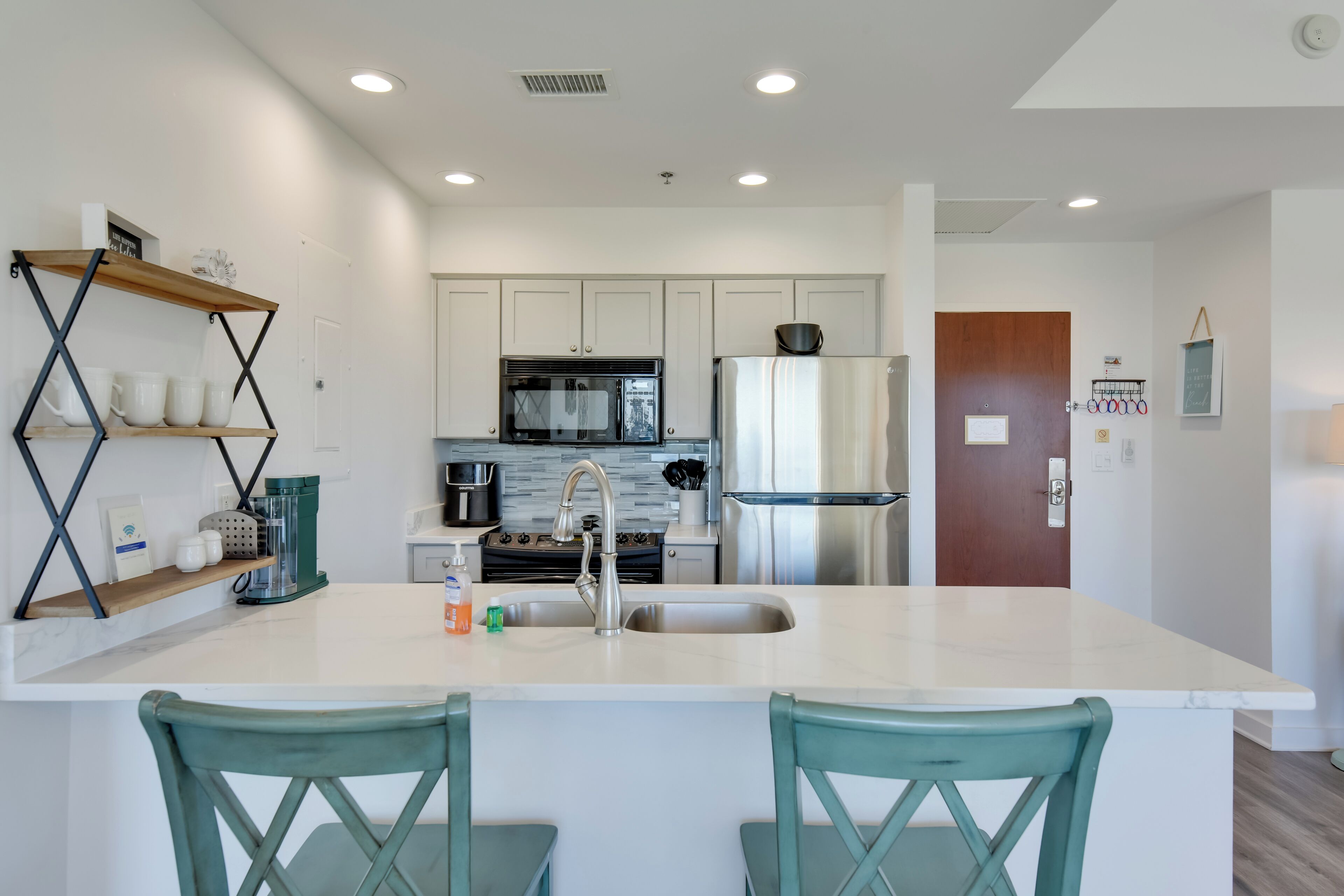 Una cocina moderna con armarios blancos, electrodomésticos de acero inoxidable y sillas color turquesa.