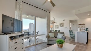 Ein modernes Wohnzimmer mit Flachbildfernseher, einem Essbereich mit Tisch und Stühlen, einer Küchenzeile und einem Balkon mit Blick auf die Stadt.