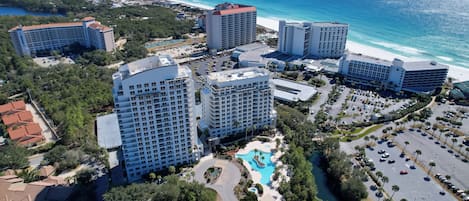 Vista aérea de un complejo hotelero con varias torres, una piscina central y acceso a la playa.