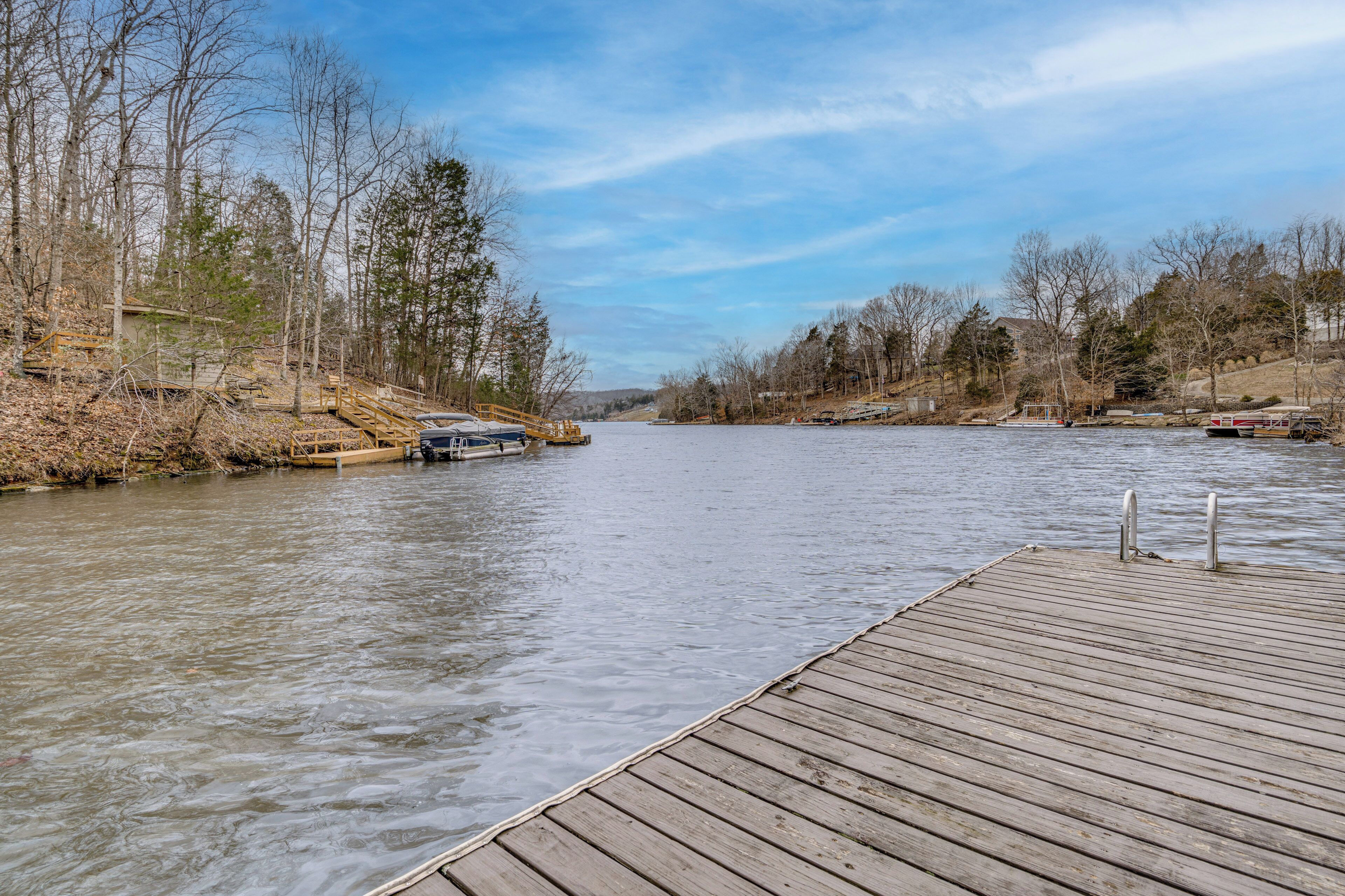 A wooden dock extending into a calm river, surrounded by trees and a clear sky.