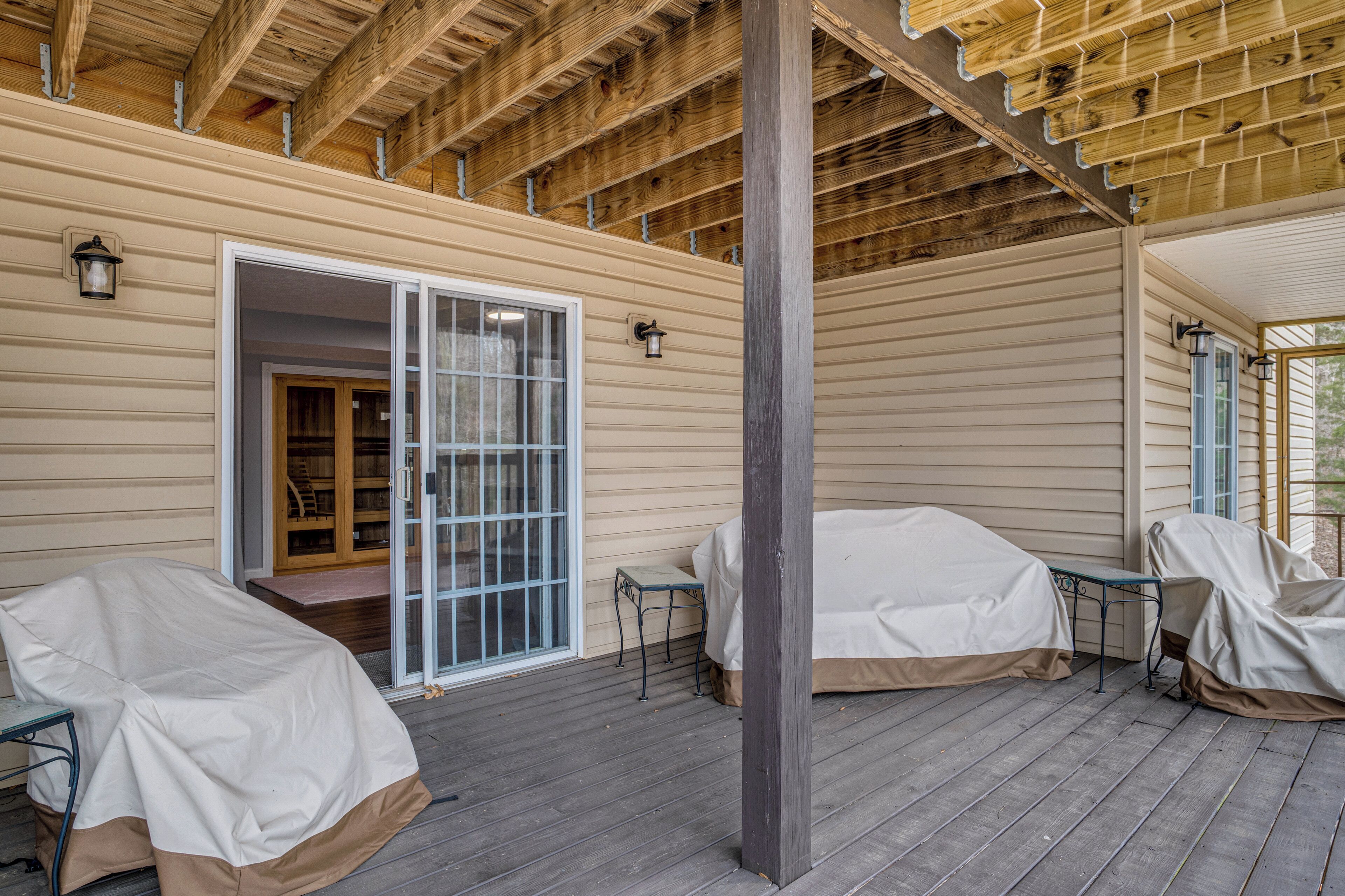 A covered outdoor area with a wooden ceiling, a sliding glass door, and covered seating.