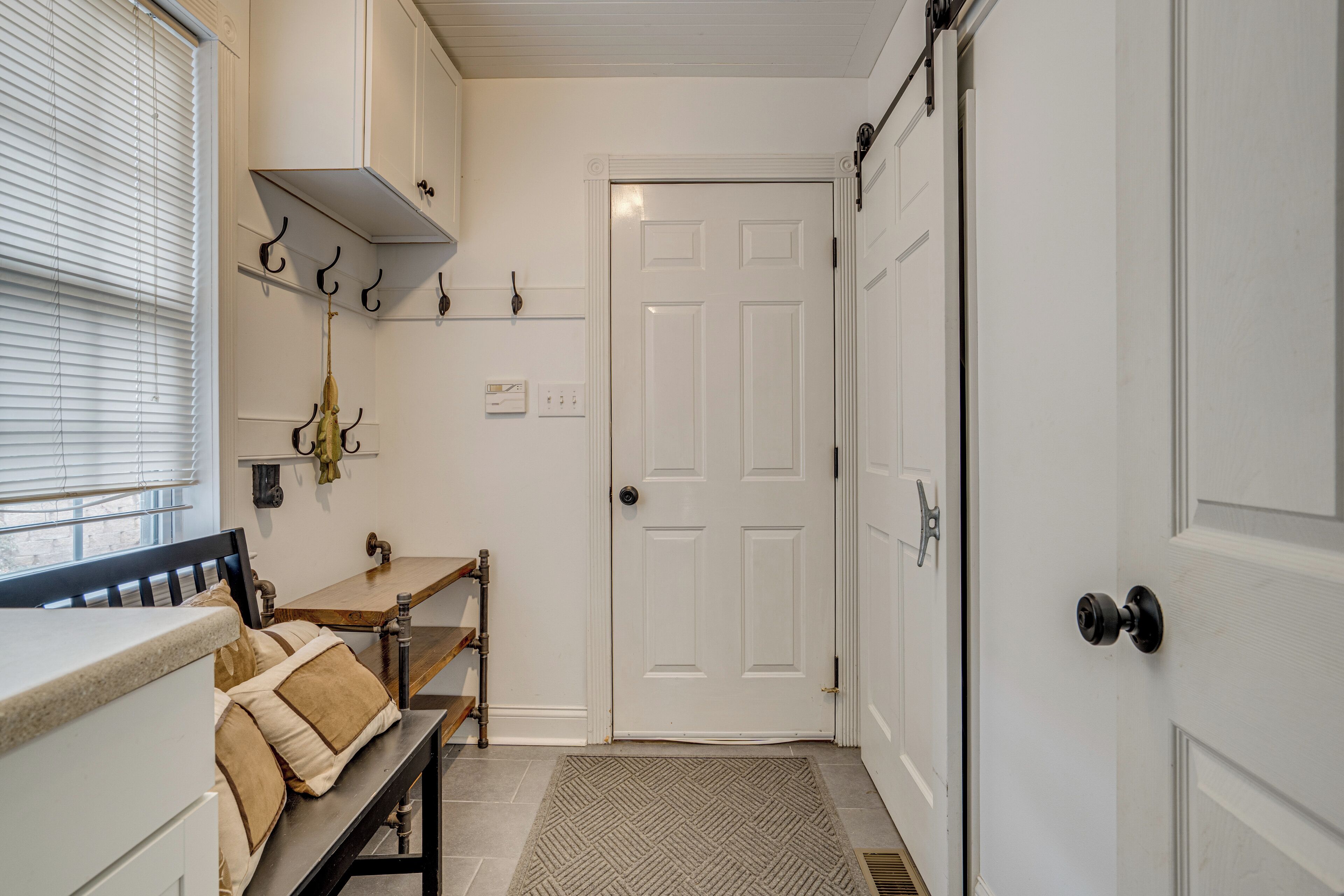 A hallway with a bench, a door, and a window with blinds.