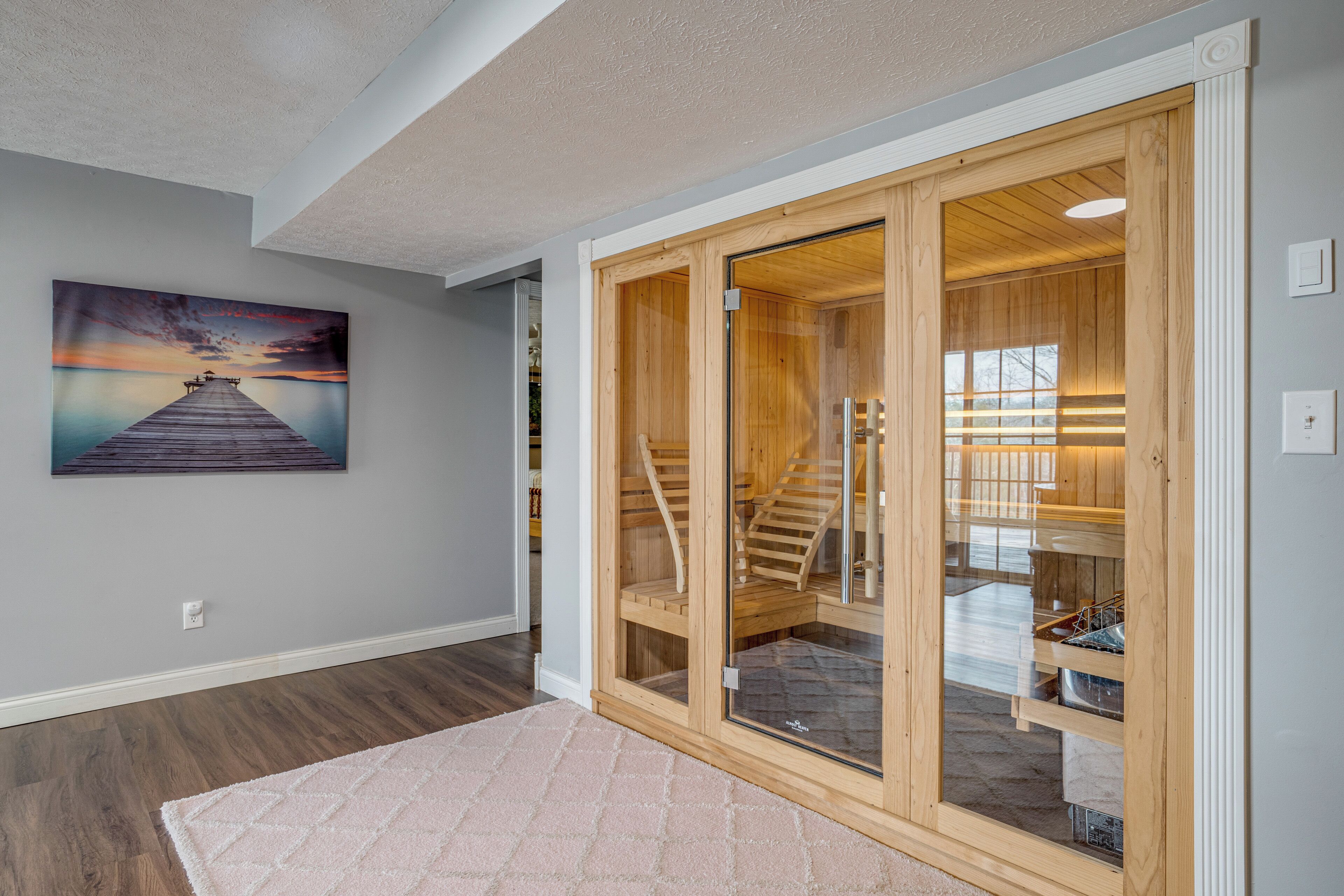 A modern interior with a wooden staircase, a glass door leading to a storage area, and a sunset painting on the wall.