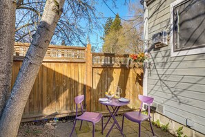 A patio with two purple chairs and a table set for two, a wooden fence, and a house with a window and an air conditioning unit. - Walk to Dtwn Ashland! Couple's Retreat w/ Yard (Ashland)