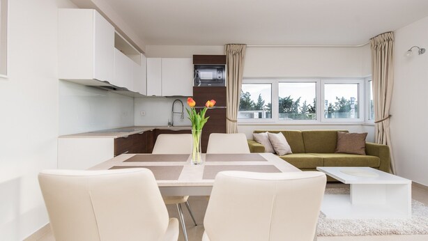A modern apartment with a dining area, a green sofa, a kitchen with a microwave, and a large window. - Sargas Suite 5 With Pool View (Novalja)