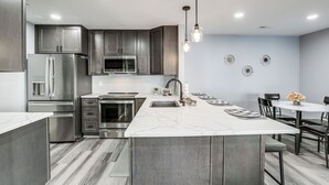 A modern kitchen with stainless steel appliances, a marble island, and a dining area with black chairs. - Easy Commute to Philly: Traveling Pros' Hub! (Levittown)