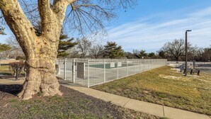 A fenced outdoor area with a tree and a building in the background. - Easy Commute to Philly: Traveling Pros' Hub! (Levittown)