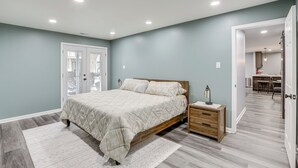 A bedroom with a bed, bedside table, and a view of the kitchen. - Easy Commute to Philly: Traveling Pros' Hub! (Levittown)
