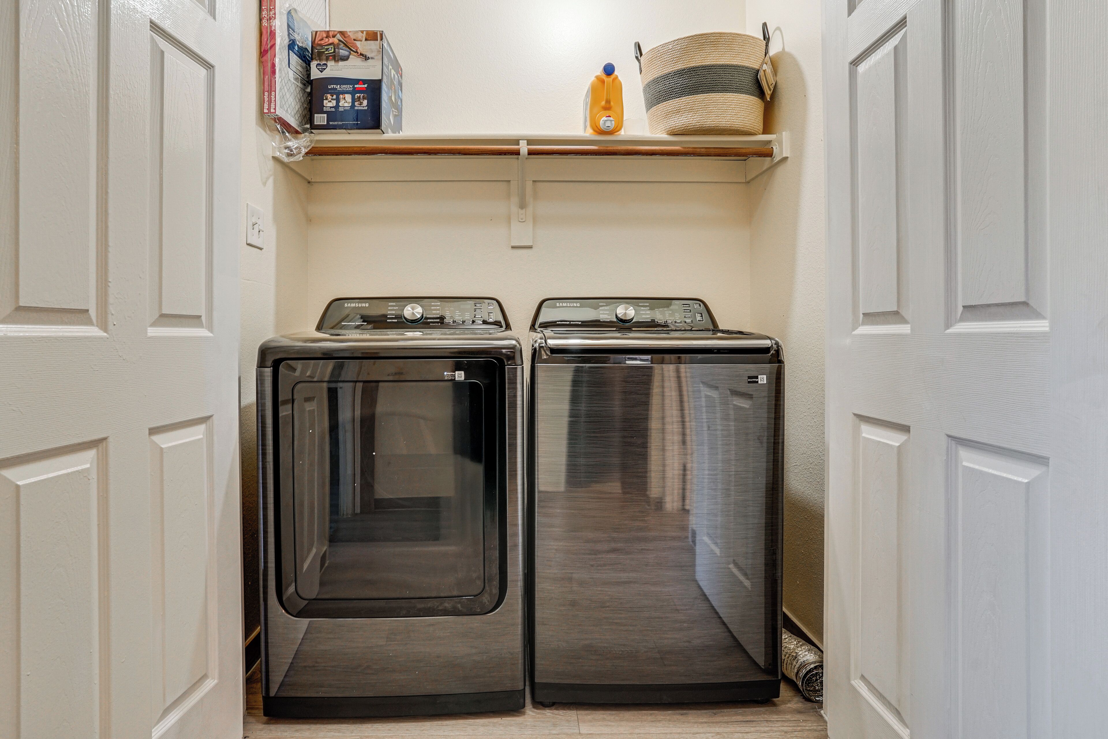 A laundry room with two front-loading washing machines and a shelf above them.