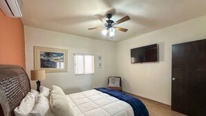 A bedroom with a bed, a ceiling fan, a TV, a door, and a window. - Serena Stay Spacious 3BR Apartment (Puerto Peñasco)