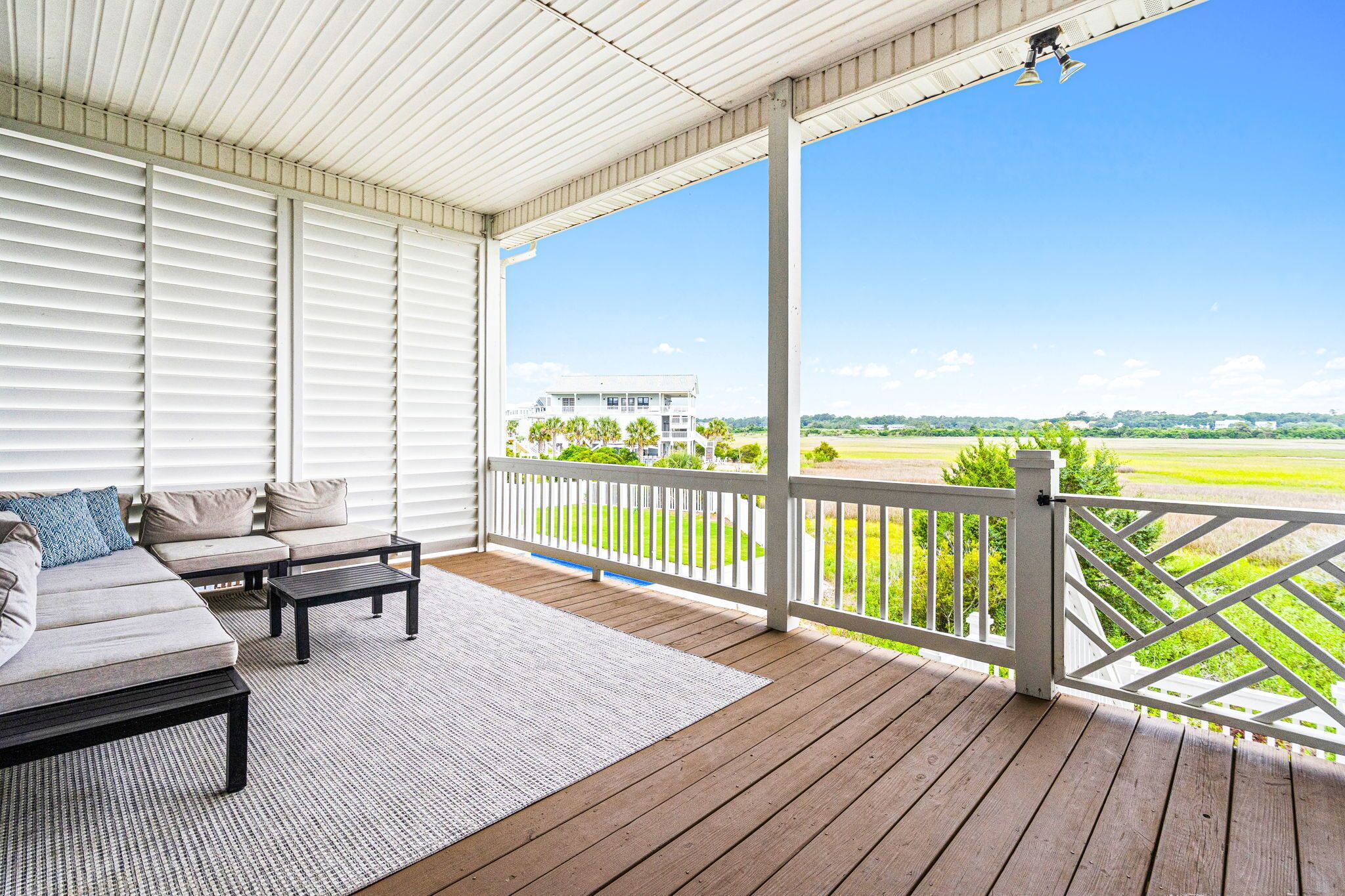 A covered porch with a sofa and coffee table, a view of a green field and a distant building.