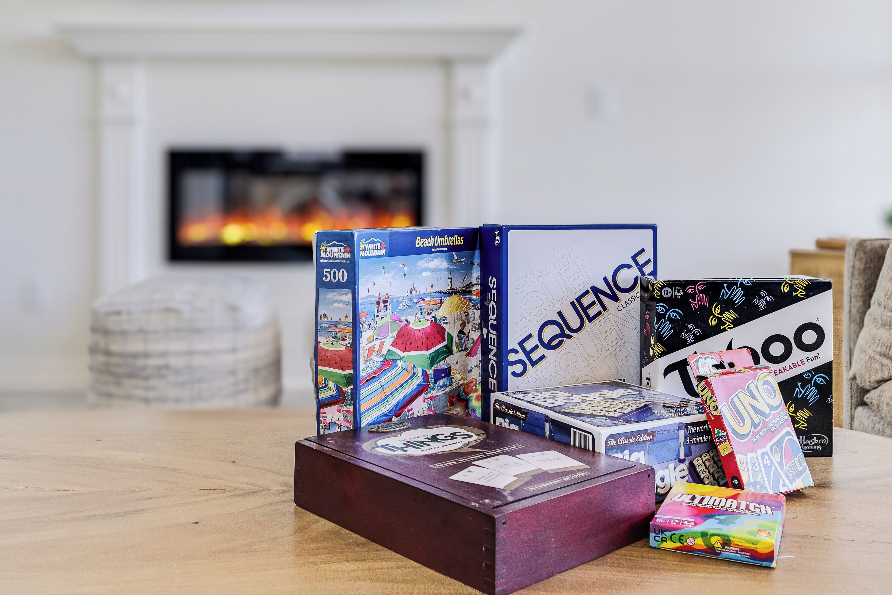 A variety of board games on a wooden table with a fireplace in the background.