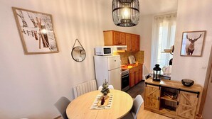 Eine kompakte Küche mit Holzausstattung, einer Mikrowelle und einem kleinen Kühlschrank. Es ist ein Esstisch mit Stühlen und eine kleine Weihnachtsstern-Deko vorhanden.