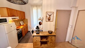 Eine kompakte Küche mit Holzschränken, einer Mikrowelle und einem Herd. Ein kleiner Tisch mit einer Laterne und einem gerahmten Bild an der Wand.