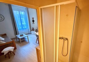 Quarto com cama, mesa pequena, cadeira, janela e área de duche.