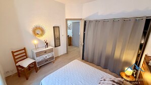 Ein Schlafzimmer mit Bett, Schminktisch, Stuhl, Spiegel und Vorhang.