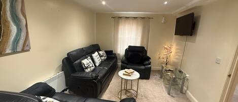 A modern living room with a black leather sofa, a black armchair, a small round table with books, and a glass coffee table.