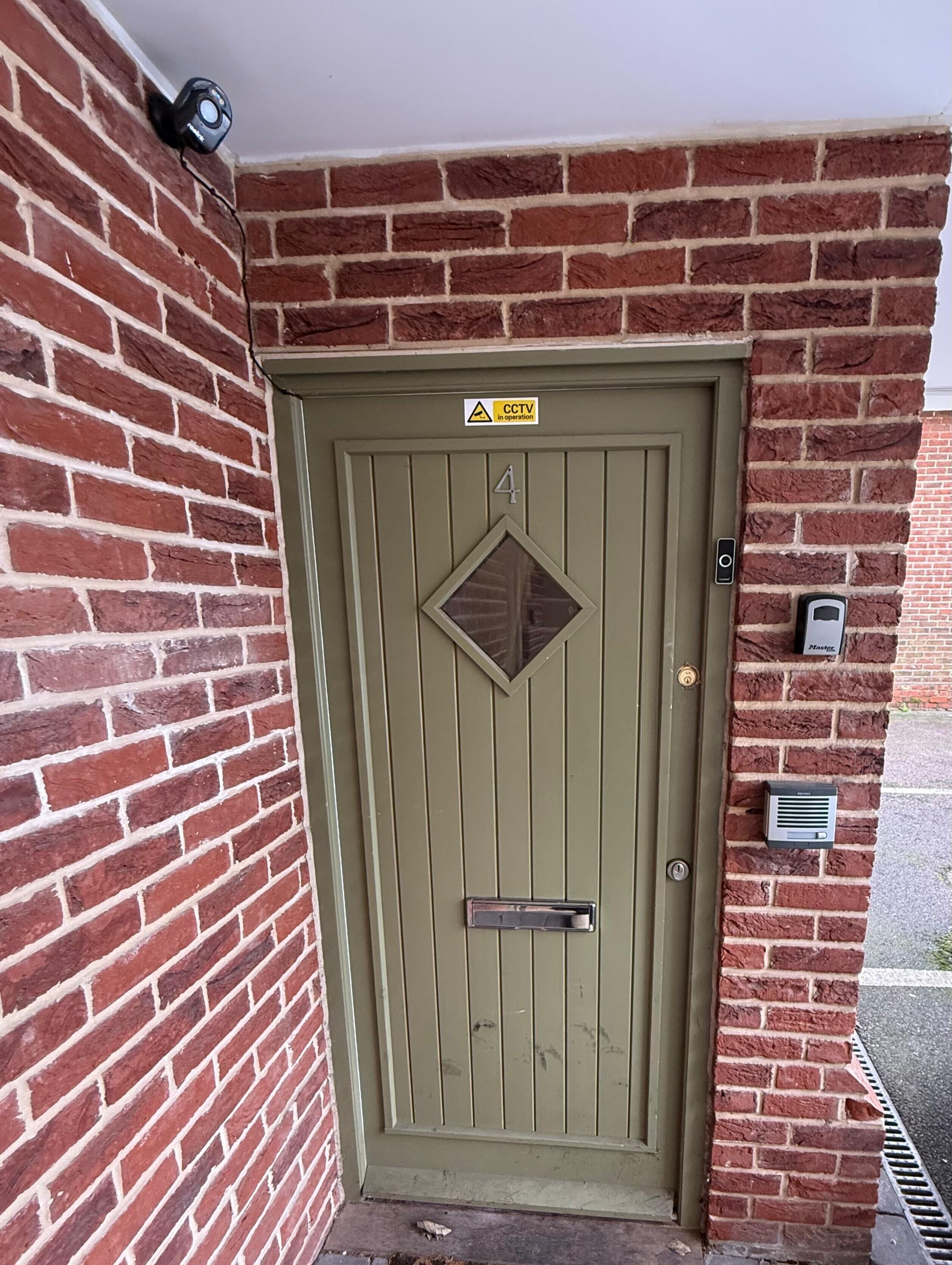 Una porta verde con un cartello per telecamere di sicurezza, una cassetta delle lettere e una targa.