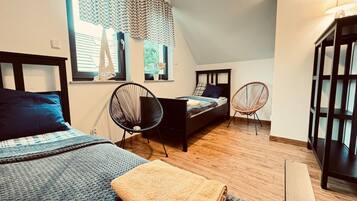 A bedroom with a bed, two chairs, a window with curtains, and a wooden floor.