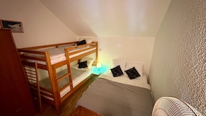 A small, dimly lit room with a bunk bed, a single bed, and a small table with a lamp. - Stay by the Hiking Trails (Mont-Dore)