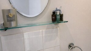 A bathroom with a white sink, a round mirror, and a glass shelf with toiletries.