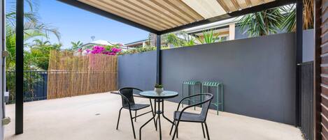 An outdoor patio with a round table and two chairs, a bamboo fence, and a view of a residential area.